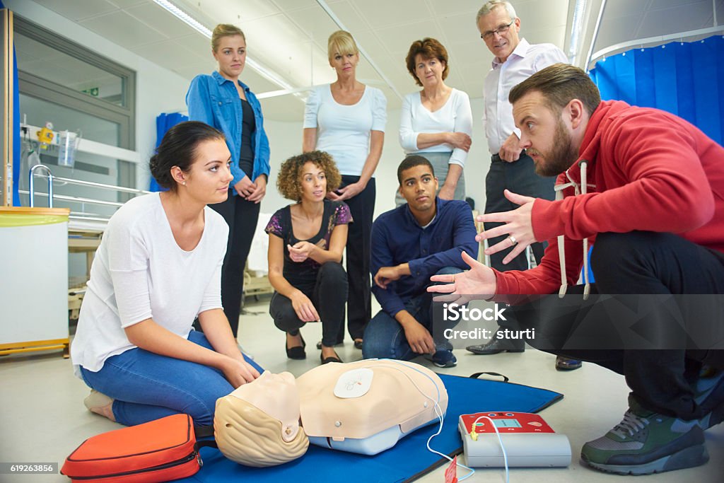 first aid training class a mixed age group listen to their tutor as he shows the procedure involved to resuscitate using a defibrillator . First Aid Stock Photo