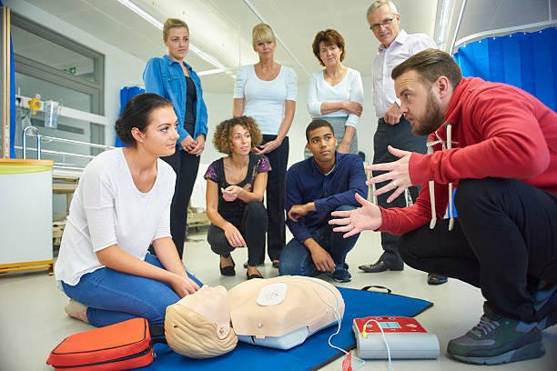 first aid training class a mixed age group listen to their tutor as he shows the procedure involved to resuscitate using a defibrillator . defibrillator photos stock pictures, royalty-free photos & images
