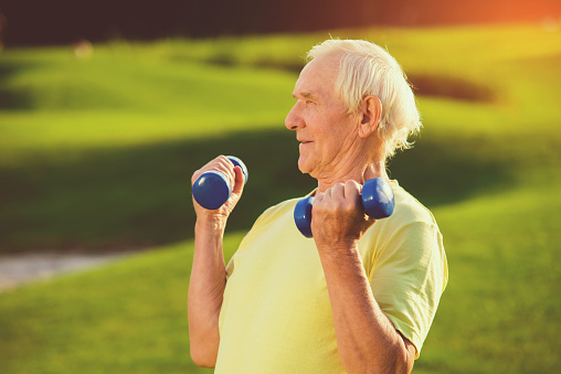 Senior man with dumbbells. Person does exercise outdoor. Be healthy and strong. Work on the muscles.
