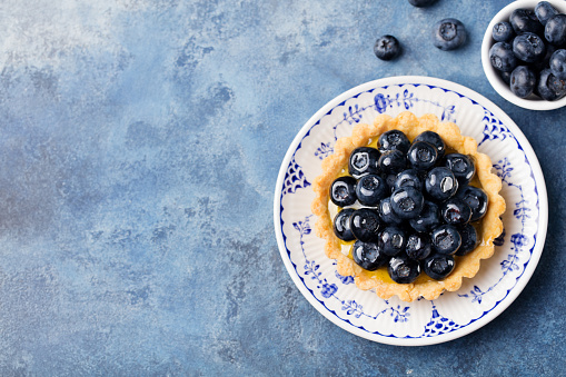 Blueberry tartlet, pie, tart with vanilla custard. Blue stone background. Top view Copy space.
