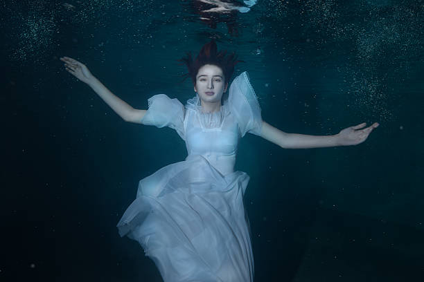 Woman in a white dress under water. Woman in white dress underwater dancing around splashes of water. immersed in their work stock pictures, royalty-free photos & images