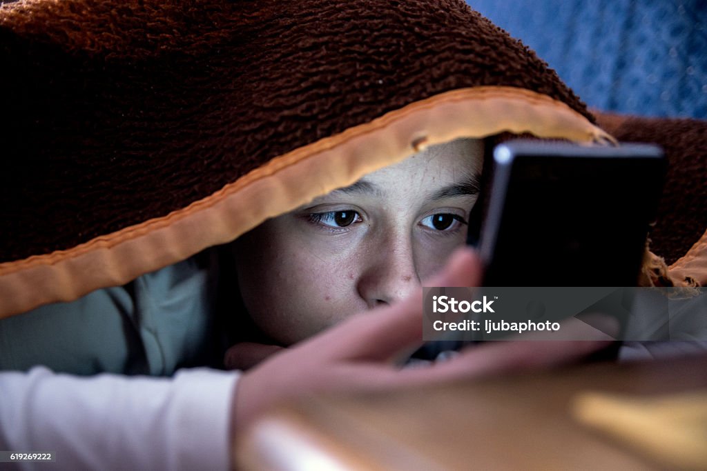 girl in bed texting on smartphone Teenager Stock Photo