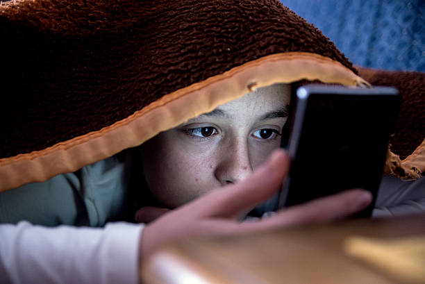 девушка в постели текстовых сообщений на смартфоне - young women teenager teenagers only adolescence стоковые фото и изображения