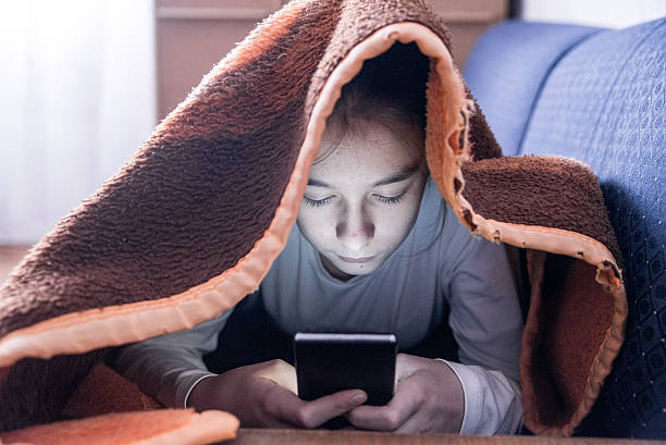 Young teen with Cellphone under Blanket on the Bed