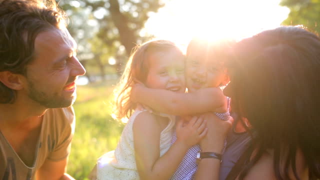 Keluarga bahagia di alam musim panas, ibu, ayah dan anak-anak dua saudara perempuan memeluk. Matahari terbenam