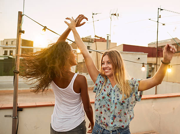 Two beautiful woman dance at sunset in a rooftop party.