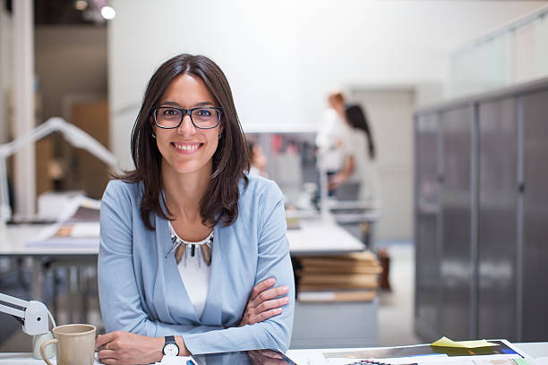 Business woman sitting at her desk in corporate office. Business woman sitting at her desk in corporate office. fine art portrait stock pictures, royalty-free photos & images