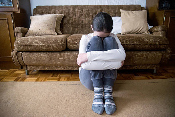 istock girl with lower head on her knee sitting beside bed 619382162