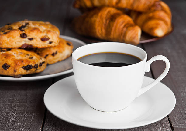 Cup of coffee with fresh scones and croissants on wooden table