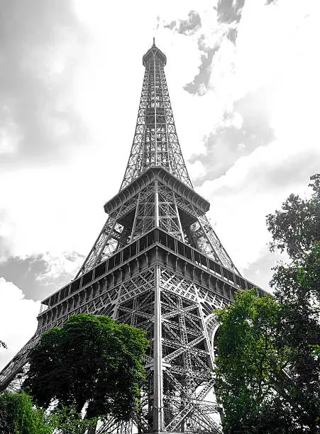 A discolored Eiffeltower in full size with green trees on the ground and shiny clouds