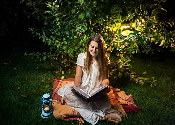 uśmiechnięta kobieta czyta książkę w ogrodzie w nocy - formal garden ornamental garden lighting equipment night zdjęcia i obrazy z banku zdjęć