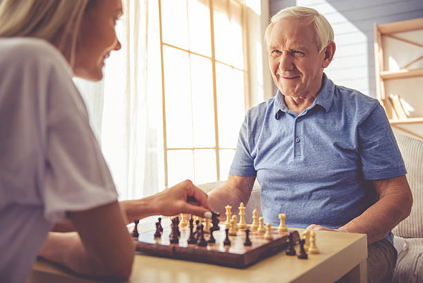 Volunteer and old people Beautiful young girl-volunteer and handsome old man are playing chess and smiling activity stock pictures, royalty-free photos & images