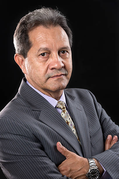 istock Older businessman wearing a suit against a black background. 619397592