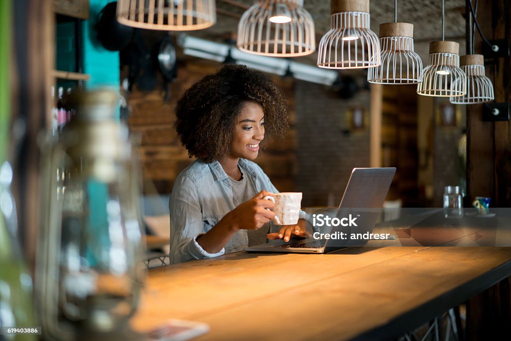 Woman working online at a cafe Casual woman working online at a cafe using a laptop computer and looking happy Coffee Shop Stock Photo