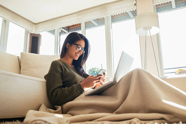 giovane donna che usa il suo smartphone e laptop - apartment window sky sun foto e immagini stock