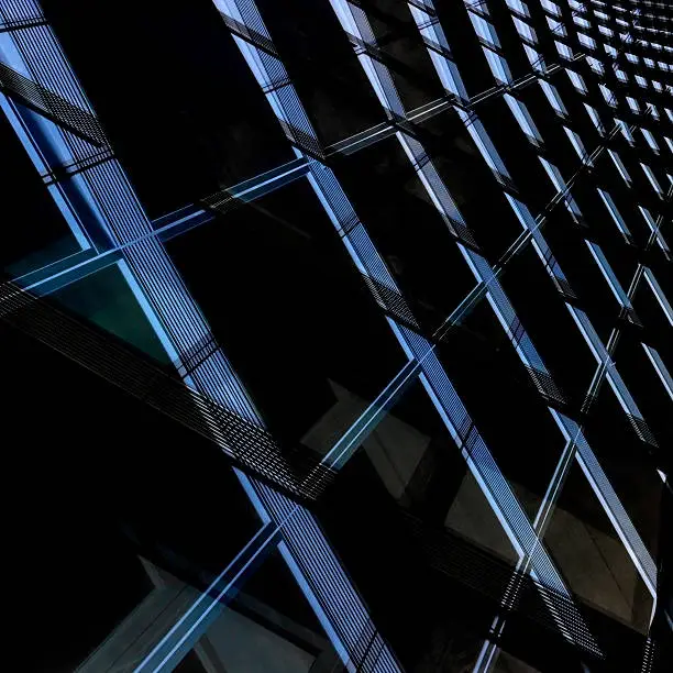 Contemporary glass architecture in the darkness. Toned tilt double exposure photo of office building with structural glazing. Realistic though fictional architectural fragment with checkered pattern.