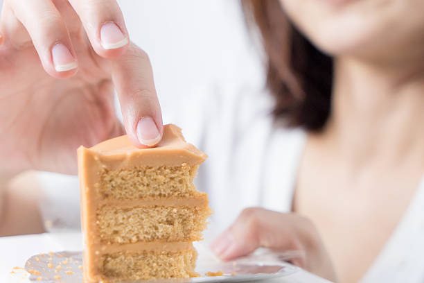 Cute Asian girl using hand to eat piece of cake.