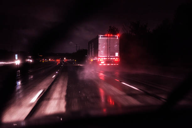 Following Rain Storm Drenched Night Expressway Speeding Semi Trailer Truck Driver POV image through the windshield of a speeding car with the windshield wipers flapping furiously during a drenching rain storm - following behind a sloppy, splashing semi tractor trailer truck on a dark night time expressway highway. Motion blur. truck rain stock pictures, royalty-free photos & images