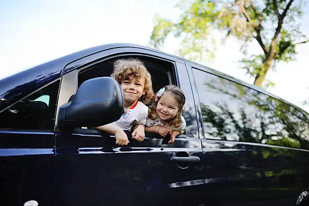 Photo of children look out from a car window