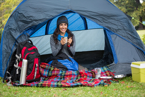 Portrait of smiling hiker having a cup of coffee in tent at forest