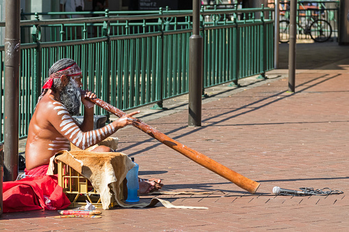 Sydney, Australia - April 20, 2016: Busker sitting and blowing didgeridoo on the ground in Sydney, Australia