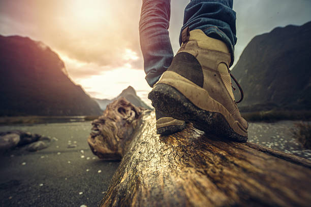 Low angle view of hiker standing on log, mountain scenery Low angle view of man's legs and hiking boots standing on tree log. Mitre peak on the background, South Island, New Zealand. mitre peak stock pictures, royalty-free photos & images