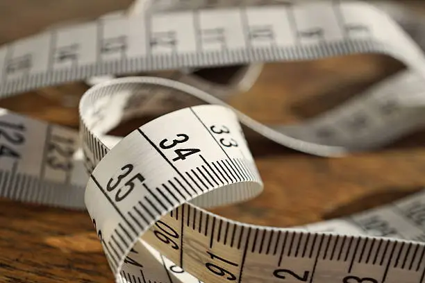 White tape measure (tape measuring length in meters and centimeters) on the wooden surface as symbol of tool used by tailor and people reducing weight during 