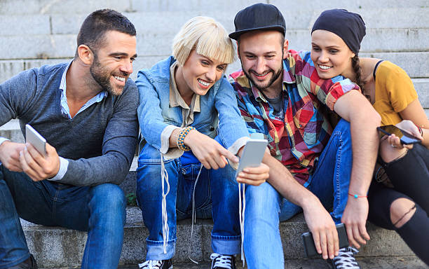 istock Smiling friends sitting on stairs and using smart phones 619529132