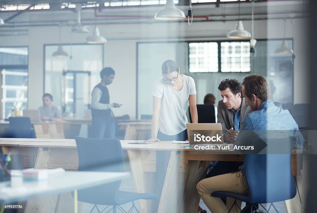 Putting there heads together on the project Shot of a group of colleagues talking together over a laptop in an office Office Stock Photo