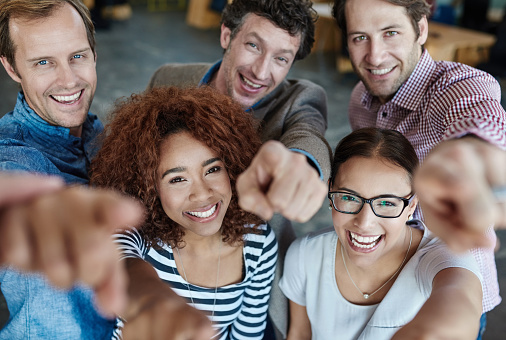 Portrait of a group of smiling coworkers pointing at the camera while standing in an office