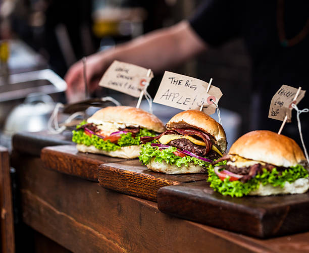 Freshly Flame Grilled Burgers at Borough Market, London, UK Square close up image of freshly flame grilled burgers in a row at Borough Market in London, UK. The burgers are all in a fresh bun, with grilled, melted cheese, red onion, lettuce and tomato. In the background we can see the out-of-focus arm of one of the stall holders who is preparing and selling the burgers. Colour image with copy space. borough market stock pictures, royalty-free photos & images