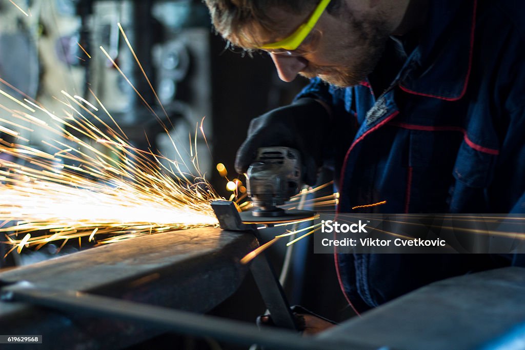 Factory worker using electric grinder in METAL INDUSTRY. Worker grinding a metal part in his workshop. Metal Stock Photo