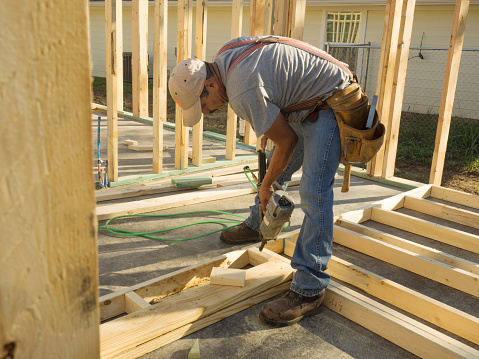 Hispanic man using a nail gun to frame a house on a construction site.