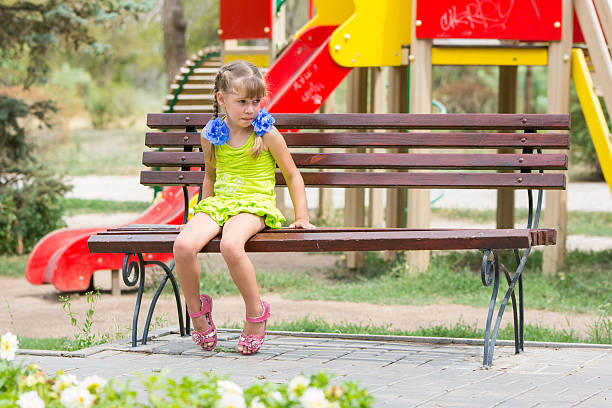Upset girl bit her lip while sitting on the bench Upset girl bit her lip while sitting on the bench on the background of the playground schoolyard fight stock pictures, royalty-free photos & images