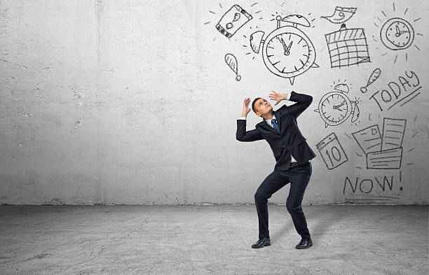 Frightened businessman shielding himself with his hands from the drawings A frightened businessman shielding himself with his hands from the drawings of calendars and clocks on the grey wall. Business and time-management. Organizing and planning. Productivity and efficiency. managing stress stock pictures, royalty-free photos & images