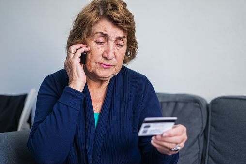 Mujer de la tercera edad que usa el teléfono móvil mientras sostiene la tarjeta de crédito photo