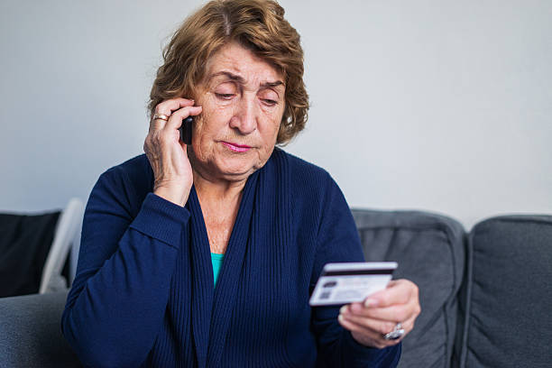 Senior woman using mobile phone while holding credit card Senior woman using mobile phone while holding credit card scam stock pictures, royalty-free photos & images