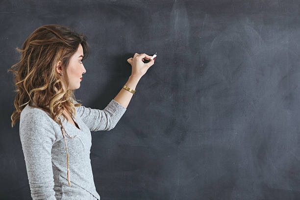 junge lehrerin schreibt an einer tafel - blackboard writing chalk teacher stock-fotos und bilder