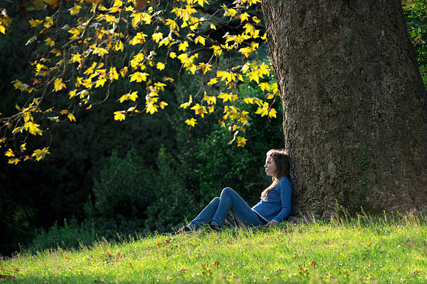 istock Girl sitting on the grass under maple tree in autumn 619660694