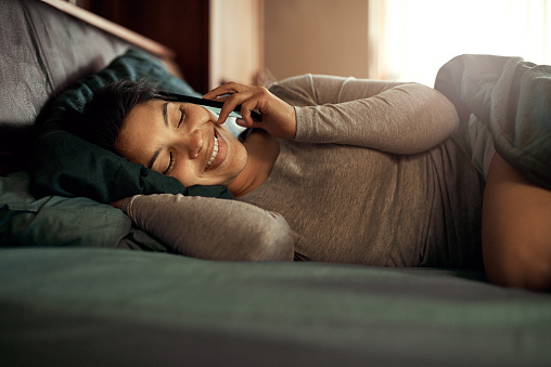 Shot of a happy young woman answering her phone while lying in bed