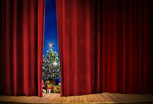 decorated Christmas tree with lights and gift boxes on red curtain stage.