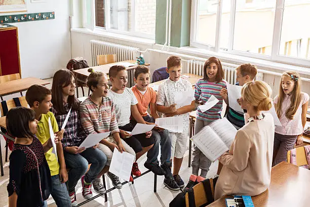 High angle view of elementary teacher practicing with group of kids during music lecture in the classroom.
