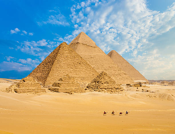 All Egypt Pyramids Camels Line Walking Wide Angle All Egyptian Pyramids from distance with row of camels walking in foreground in Giza, Cairo, Egypt. Wide telephoto shot plenty of copy space. great pyramid of khufu stock pictures, royalty-free photos & images