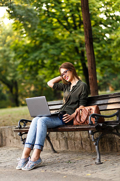 istock Young female student in park with laptop. 619728346