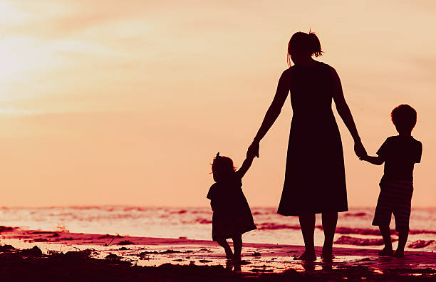 istock mother and two kids walking on beach at sunset 619731070