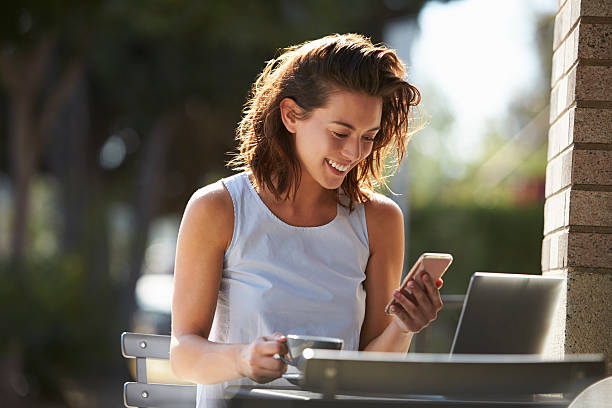 カフェの外でスマートフォンとラップトップを使う若い女性 - laptop cafe coffee coffee shop ストックフォトと画像