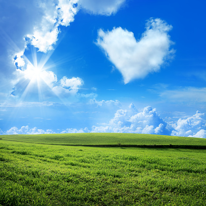 green landscape and heart shaped cloud over blue sky with clouds and sunbeam