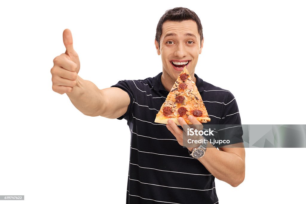 Joyful young man eating pizza slice and giving thumb up Joyful young man eating a slice of pizza and giving a thumb up isolated on white background Holding Stock Photo