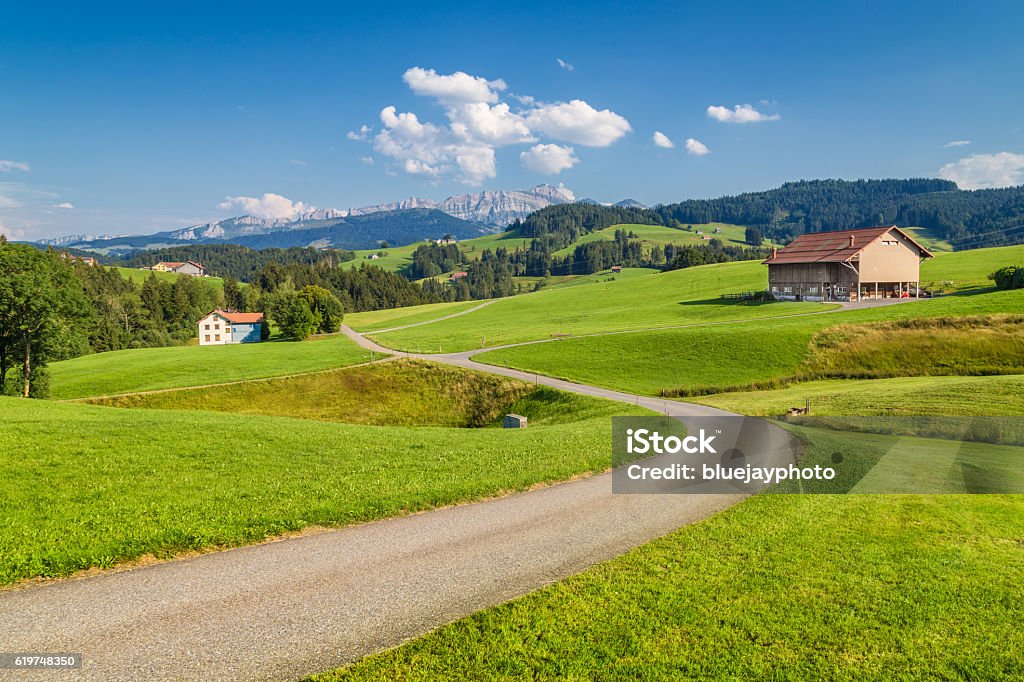 Mountain road in the Alps, Appenzellerland, Switzerland Beautiful view of idyllic mountain scenery in the Alps with green meadows and famous Saentis summit in the background on a sunny day with blue sky and clouds in summer, Appenzellerland, Switzerland Farm Stock Photo