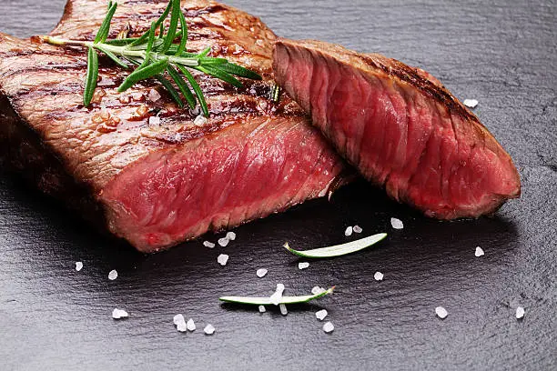 Grilled beef steak with rosemary, salt and pepper on black stone plate